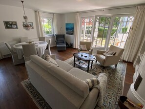 A living room with a sofa, armchairs, a coffee table, and a dining area with a table and chairs. - Palais am Südstrand - Whg. 1 - Apartment Palais am Südstrand: Sauna, (Wyk auf Föhr)