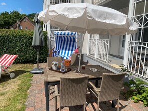 An outdoor patio with wicker furniture, a table with a tray, and a striped chair. - Palais am Südstrand - Apt. 1 - Palais am Südstrand Apartment: Sauna, (Wyk auf Föhr)