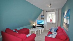 A living room with red sofas, a TV, and a small white table. - Bredland 2a - Whg. 5 - Holiday apartment in Nieblum: 52 m², terrace & only 200 m to the beach (Nieblum)