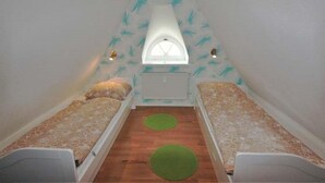 A small, triangular attic room with two single beds, a window, and a radiator. - Bredland 2a - Whg. 5 - Holiday apartment in Nieblum: 52 m², terrace & only 200 m to the beach (Nieblum)