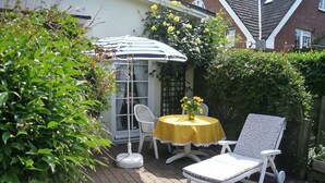 Un patio exterior con mesa y sillas, una sombrilla blanca y un mantel amarillo.