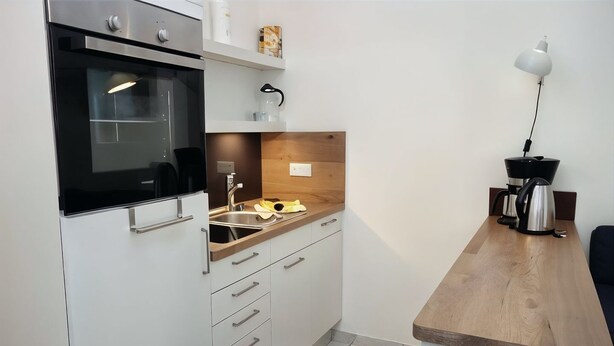 Una cocina moderna con horno empotrado, lavamanos y cafetera sobre una encimera de madera.