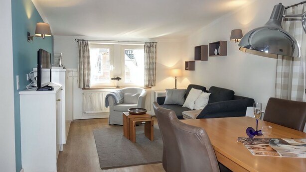 A modern living room with a sofa, a dining table, and a kitchen area with a fridge. - Hallig Hooge - Whg. 6 - Hbg. Hallig - Non-smoking vacation apartment on Föhr, (Wyk auf Föhr)