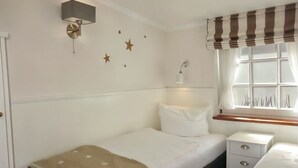 A bedroom with a bed, bedside table, lamp, window with curtains, wall stars, and a wall-mounted light fixture. - Hallig Hooge - Whg. 6 - Hbg. Hallig - Non-smoking vacation apartment on Föhr, (Wyk auf Föhr)