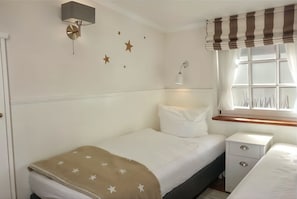 A bedroom with a bed, bedside table, lamp, window with curtains, wall stars, and a wall-mounted light fixture. - Hallig Hooge - Whg. 6 - Hbg. Hallig - Non-smoking vacation apartment on Föhr, (Wyk auf Föhr)