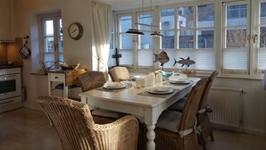 Et spiseområde med et hvidt bord, fletstole, et ur og dekorative fisk på vindueskarmen.