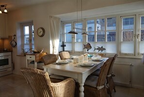 A dining area with a white table, wicker chairs, a clock, and decorative fish on the windowsill. - Eulenkamp 8 a - DHH left - Holiday home Eulenkamp 8a: DHH left, 200 m to the beach (Wyk auf Föhr)