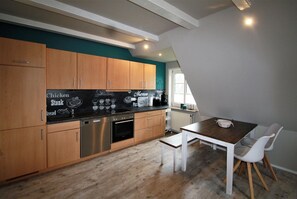A modern kitchen with wooden cabinets, a black countertop, and a dining area with a table and chairs. - Nis Puk - FW Hooge - Space for up to 5 people, garden & 500 m to the beach (Utersum)