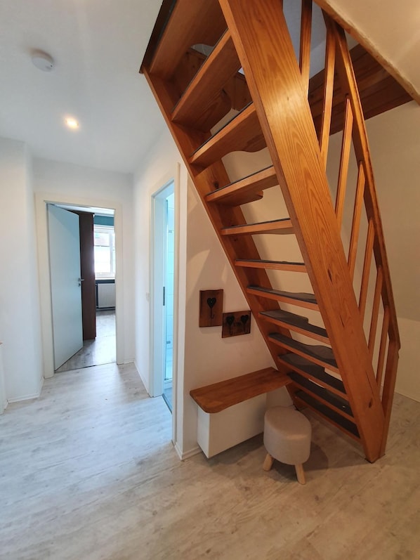 A modern interior with a wooden spiral staircase, a small stool, and a hallway leading to another room. - Nis Puk - FW Hooge - Space for up to 5 people, garden & 500 m to the beach (Utersum)