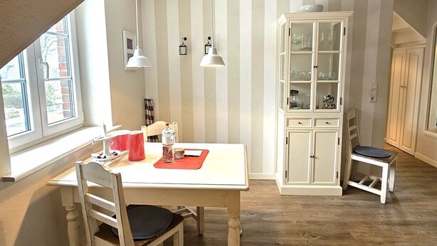 Een eetruimte met een witte tafel, twee stoelen, een kast met glazen deuren en een hangende lamp.