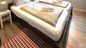 Een slaapkamer met twee bedden, een raam met gordijnen, een nachtkastje met een lamp en een geruit tapijt.