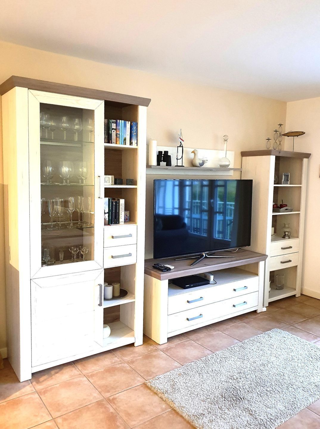 Een woonkamer met een televisie, glazen, boeken en decoratieve items op planken.