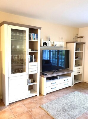A living room with a TV, glassware, books, and decorative items on shelves. - Palais am Südstrand - Whg. 2 - Holiday apartment on the south beach: close to the beach and (Wyk auf Föhr)