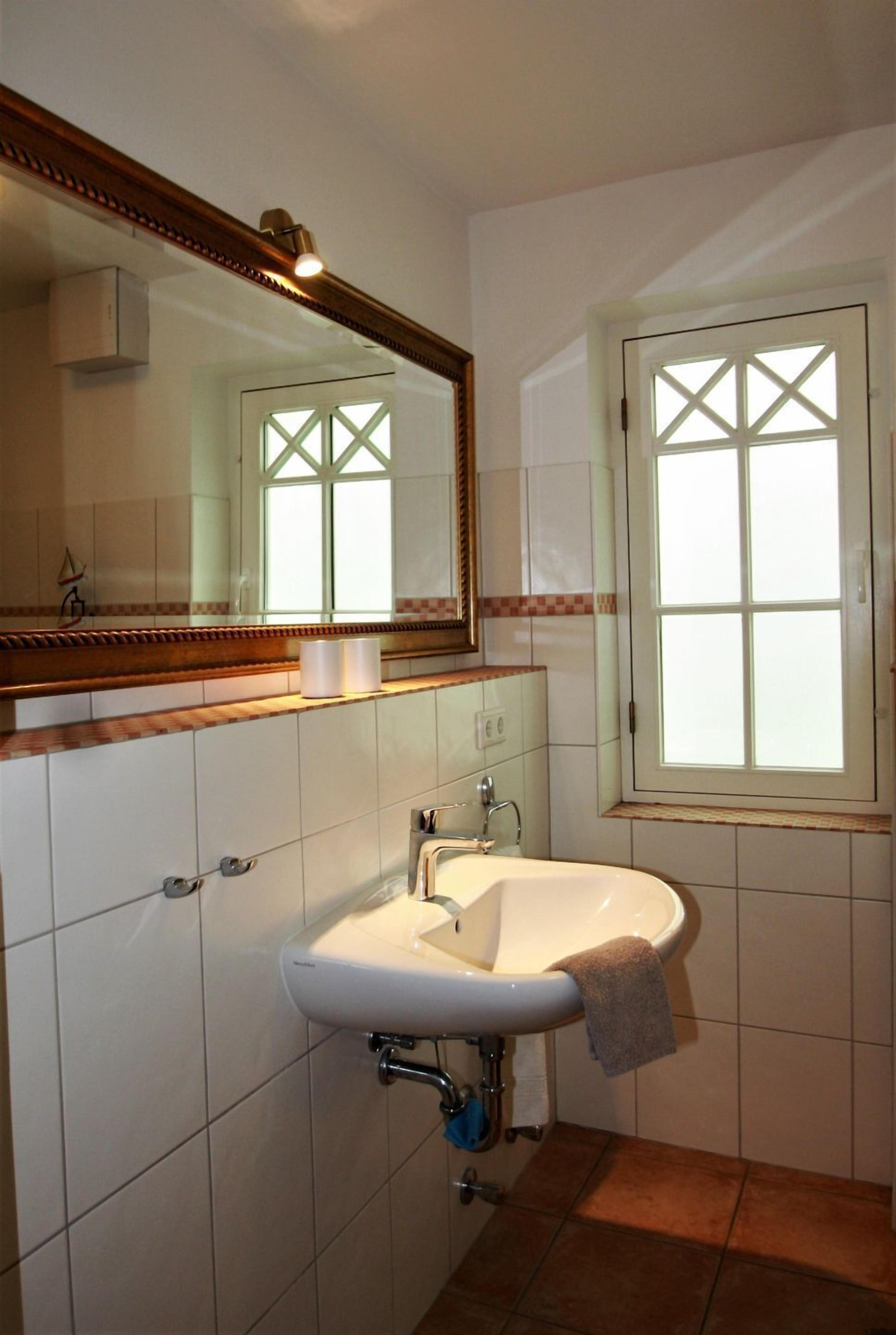 Ein Badezimmer mit einem weißen Waschbecken, einem Spiegel und einem Fenster mit Kreuzmuster.