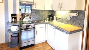 Una cocina compacta con armarios blancos, estufa de acero inoxidable, lavavajillas y encimera de granito.