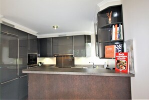 A modern kitchen with dark cabinets, a stainless steel range hood, and a built-in bookshelf with books. - Boldixumer Str. 35 - Ground floor - Holiday apartment in Wyk auf Föhr: Garden, terrace & (Wyk auf Föhr)