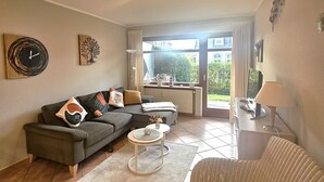 Un salón con sofá, sillón, mesa de centro y vistas a través de un ventanal.