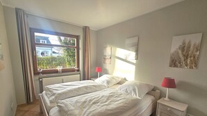 Un dormitorio con dos camas, una ventana con cortinas, una mesita de noche con lámpara y una obra de arte en la pared.