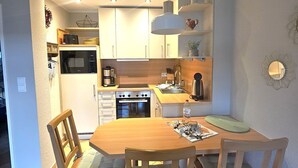 Una cocina compacta con electrodomésticos modernos, un comedor con sillas de madera y una lámpara colgante.