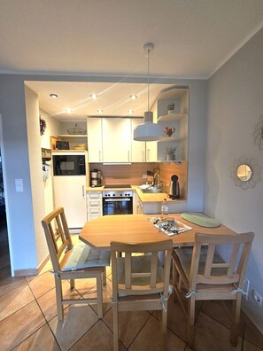 A compact kitchen with modern appliances, a dining area with wooden chairs, and a pendant light. - Schatzinsel, Whg. 1 - Holiday apartment Schatzinsel Whg. 1 on Föhr - Terrace & (Wyk auf Föhr)