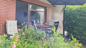 Un patio con una mesa, sillas y un paraguas grande, además de un muro de ladrillo.
