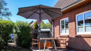 A patio with a table and chairs, a large umbrella, and a brick house. - Nis Puk _FW Habel (ground floor) - vacation apartment in Utersum: 50 m² with terrace, close to the beach (Utersum)