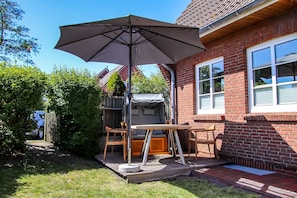 Eine Terrasse mit Tisch und Stühlen, einem großen Sonnenschirm und einem Ziegelhaus.