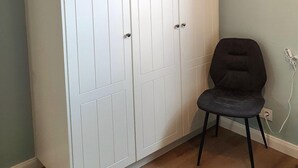 Ein Zimmer mit einem weißen Kleiderschrank, einem grauen Sessel und einer Steckdose.