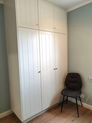 A room with a white wardrobe, a grey chair, and a wall socket. - Haus am Walde - Ground floor - Bright vacation apartment in Haus am Walde on the ground floor, 380 m to the (Wyk auf Föhr)