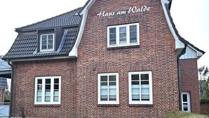 Ein rotes Backsteingebäude mit der Aufschrift 'Hans am Walde' an der Fassade, zahlreichen Fenstern und einem geneigten Dach.