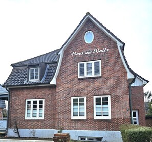 A red brick building with the text 'Hans am Walde' on the facade, multiple windows, and a sloped roof. - Haus am Walde - Ground floor - Bright vacation apartment in Haus am Walde on the ground floor, 380 m to the (Wyk auf Föhr)