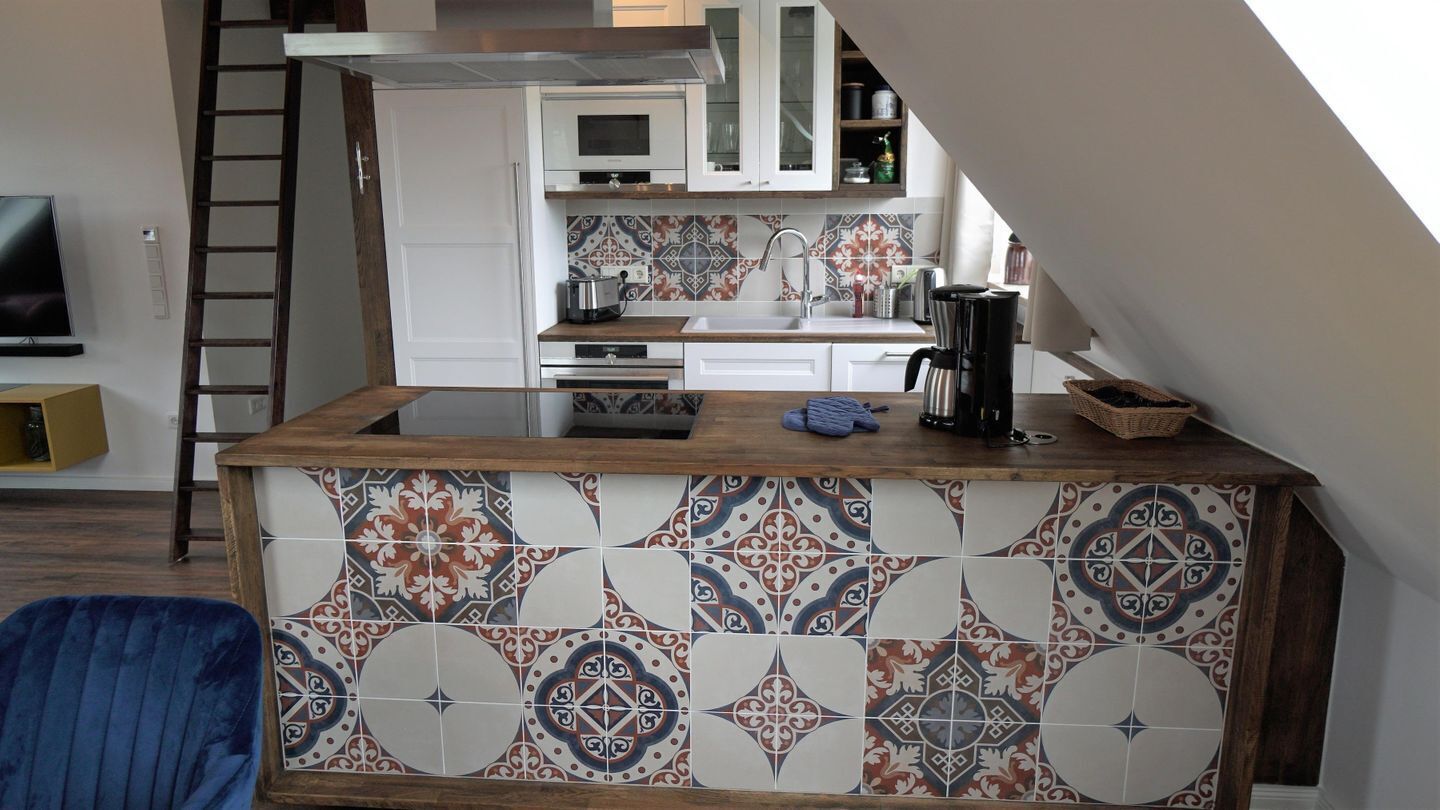 A kitchen with a tiled backsplash, a wooden countertop, and a microwave above it.