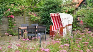 A garden with a wooden pergola, a dining table with chairs, and a covered chair. - Seestern - Holiday apartment Seestern in Wyk on Föhr - 80 m², terrace & garden (Wyk auf Föhr)
