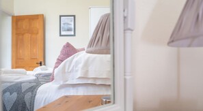 Ein Schlafzimmer mit Bett, Kissen, Decke, einem Holzkopfende, einer Tür und einem gerahmten Bild an der Wand.
