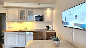 A modern kitchen with wooden cabinets, a built-in oven, and a dining area with wicker chairs. - Mühlenblick - Apartment Mühlenblick: 60 m² near the beach in Wyk auf Föhr (Wyk auf Föhr)
