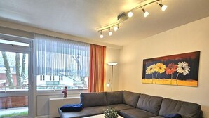 A modern living room with a grey sofa, a white coffee table, and a painting of flowers on the wall. - Mühlenblick - Apartment Mühlenblick: 60 m² near the beach in Wyk auf Föhr (Wyk auf Föhr)