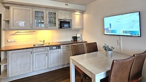 A modern kitchen with white cabinetry, a dining table with chairs, and a flat-screen TV mounted on the wall. - Mühlenblick - Apartment Mühlenblick: 60 m² near the beach in Wyk auf Föhr (Wyk auf Föhr)