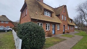 Et traditionelt murstenshus med stråtækt tag, en belagt indkørsel og en velplejet hæk.