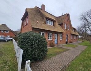 A traditional brick house with a thatched roof, a paved driveway, and a well-maintained hedge. - Am Museum - Apartment 1 - Holiday apartment Am Museum 1: Terrace, garden, WLAN & (Alkersum)