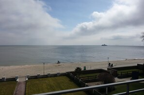 A coastal view with a beach, a ship in the distance, and a grassy area with a fence. - Strandperle - Apartment Strandperle with sea view directly on the beach in Wyk (Wyk auf Föhr)