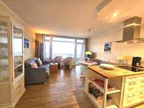 A modern living room with a sofa, chairs, a coffee table, and a dining area with a table and chairs. - Strandperle - Apartment Strandperle with sea view directly on the beach in Wyk (Wyk auf Föhr)
