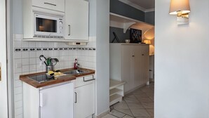 Een keuken met witte kastjes, een magnetron, een spoelbak met keukengerei en een trap naar een ander niveau.