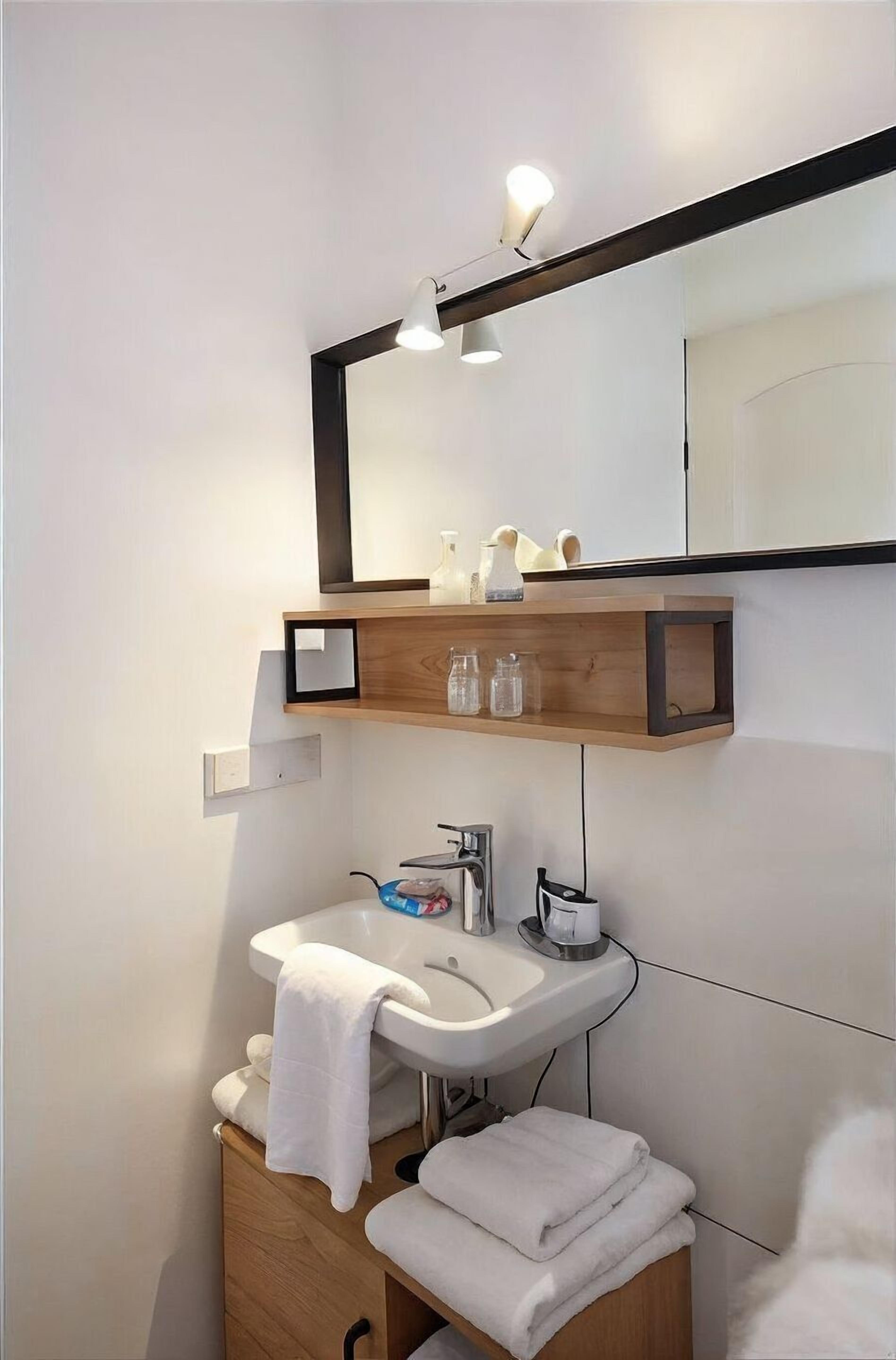 Un bagno moderno con un lavandino bianco, uno specchio e una mensola in legno con articoli da toilette.