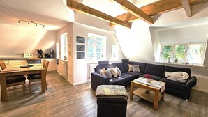 Ein geräumiger Wohnbereich mit einem Holzesstisch, einer dunkelgrauen Sofagarnitur und einem Couchtisch.