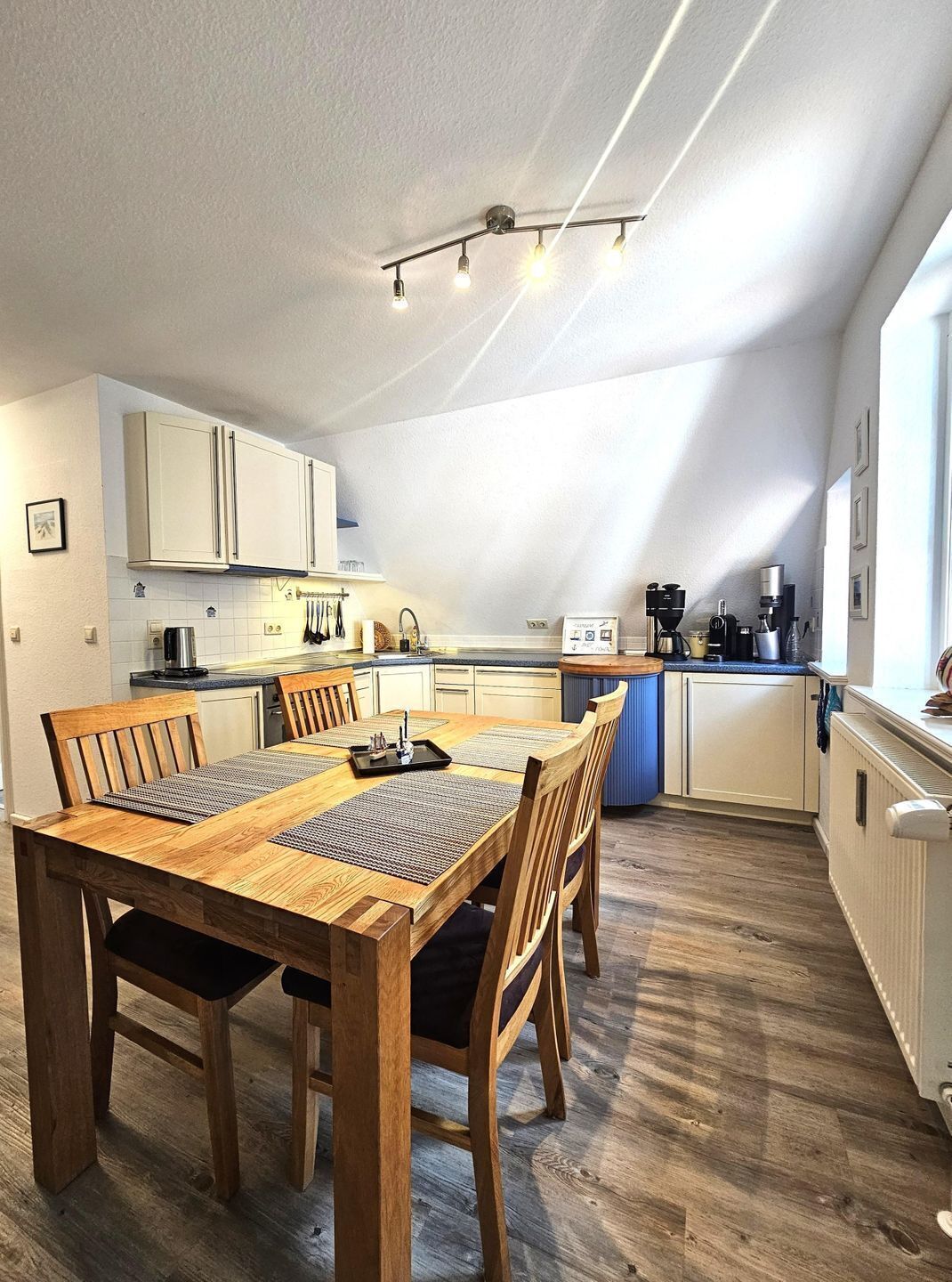 A modern kitchen with a dining area, featuring a wooden table and chairs, a kitchen island, and a sloped ceiling.