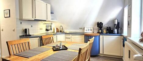 A modern kitchen with a dining area, featuring a wooden table and chairs, a kitchen island, and a sloped ceiling.