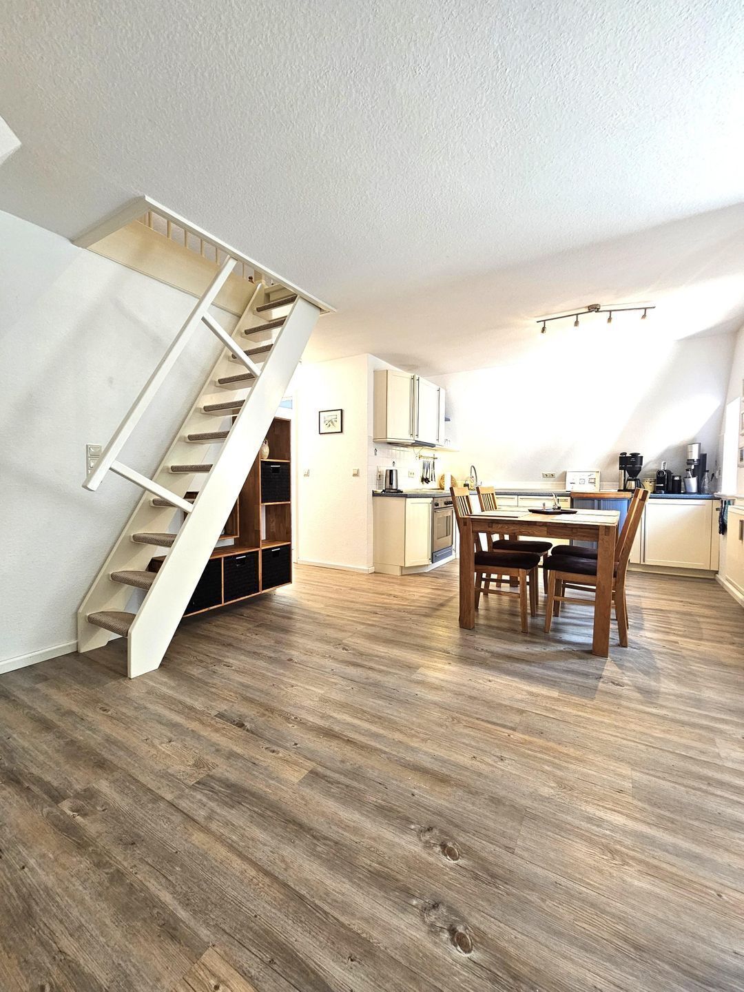 Een moderne keuken met een eethoek, houten vloeren en een trap.