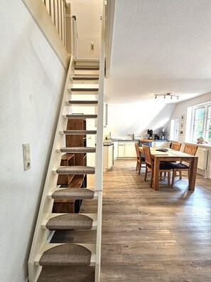 Una escalera conduce a un comedor con piso de madera y una cocina al fondo.