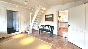 A spacious living area with a staircase, a bench, and a kitchen visible through an open door. - Ilskes Hus - Detached thatched house with garden, terrace & e-charging station (Oevenum)