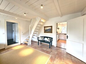 A spacious living area with a staircase, a bench, and a kitchen visible through an open door. - Ilskes Hus - Detached thatched house with garden, terrace & e-charging station (Oevenum)